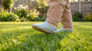 Un enfant portant des chaussures en cuir souple bleu clair marche sur une pelouse verdoyante.